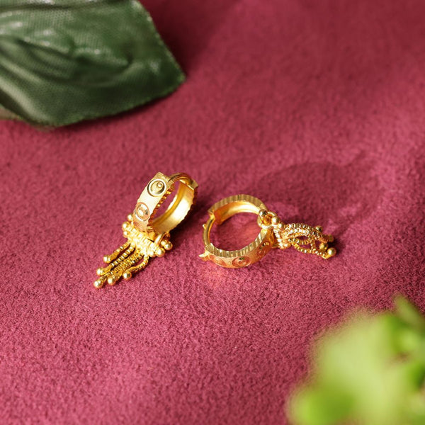 Gold hoop earrings with intricate designs on a pink fabric background
