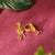 Gold hoop earrings with intricate designs on a pink textured surface