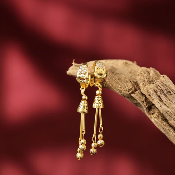 Gold earrings with dangling beads on a wooden branch against a red background