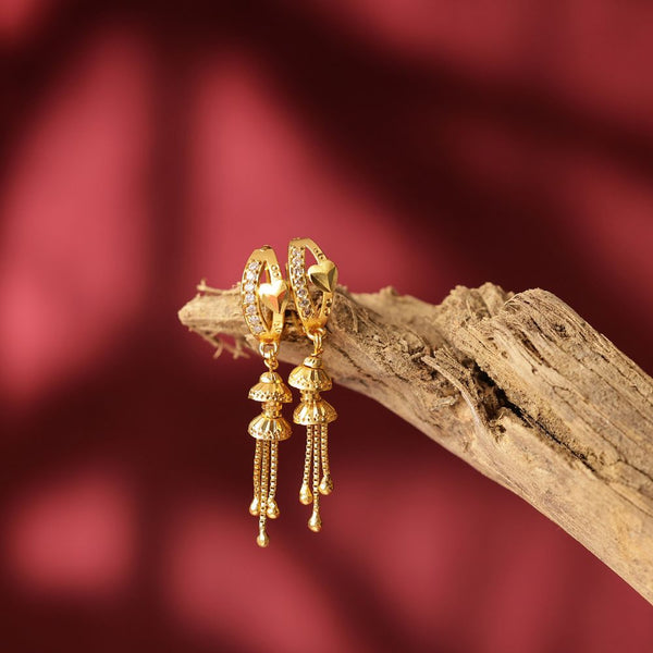 Gold earrings with dangling designs on a wooden branch against a red background