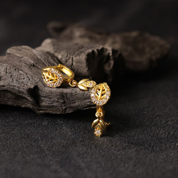 Gold earrings with leaf design on a dark surface